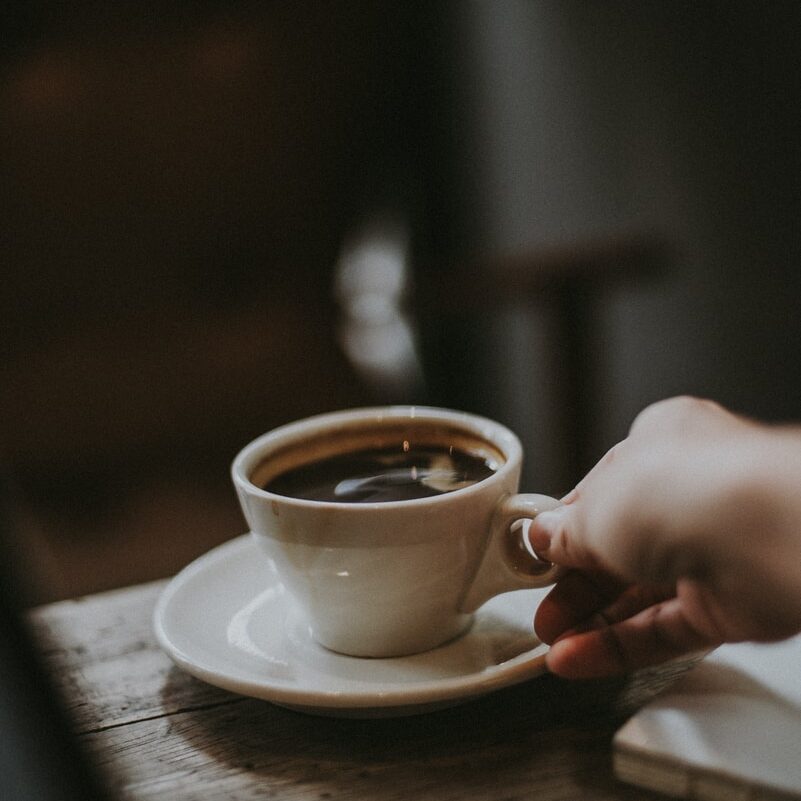 person holding white ceramic cup with liquid